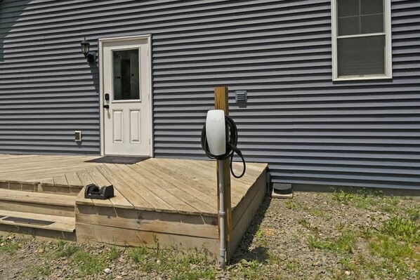 Una casa con terraza de madera, una puerta blanca y un cuadro eléctrico en la pared.