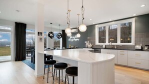 Une cuisine moderne dotée d’un îlot central, de tabourets de bar, de luminaires suspendus et offrant une vue sur l’extérieur.