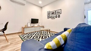 A modern living room with a blue sofa, a TV on a wooden stand, and a patterned rug. - Stylish Apt Off The Sea Front (Il-Gzira)