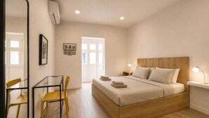 A bedroom with a wooden bed, a desk with a chair, a mirror, and a door leading outside. - Stylish Apt Off The Sea Front (Il-Gzira)