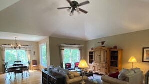 A spacious living room with hardwood flooring, a ceiling fan, a dining area with a table and chairs, and a seating area with sofas and a coffee table.