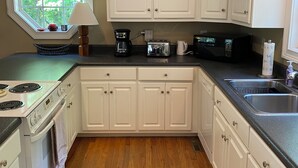 A kitchen with white cabinets, a stove, a microwave, and a coffee maker.