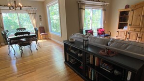 A spacious living room with a wooden floor, a dining area with a table and chairs, and a large bookshelf.