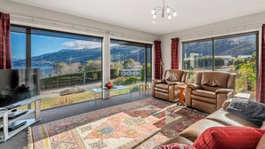 Un salon spacieux doté de grandes fenêtres, d’un téléviseur à écran plat, de canapés en cuir et d’un tapis à motifs.