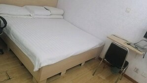 A small, neatly made bed with white linens, a wooden headboard, and a small desk with a chair beside it. - Fushun Yuanxiang Hotel (Fushun)