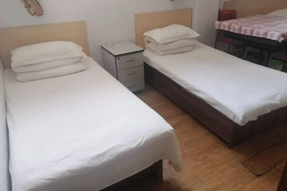 A room with two single beds, a small bedside table with drawers, and a desk with a chair.