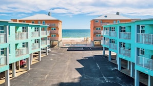 A beachfront hotel with two-story buildings, a parking area, and a view of the ocean.