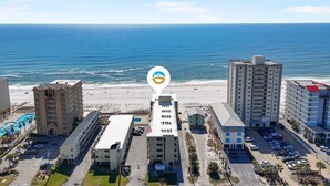A coastal hotel with multiple buildings, a parking lot, and a beach in the background.