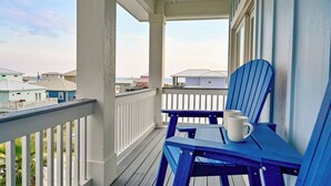 A balcony with a white railing, blue chairs, and a white mug on one of the chairs.