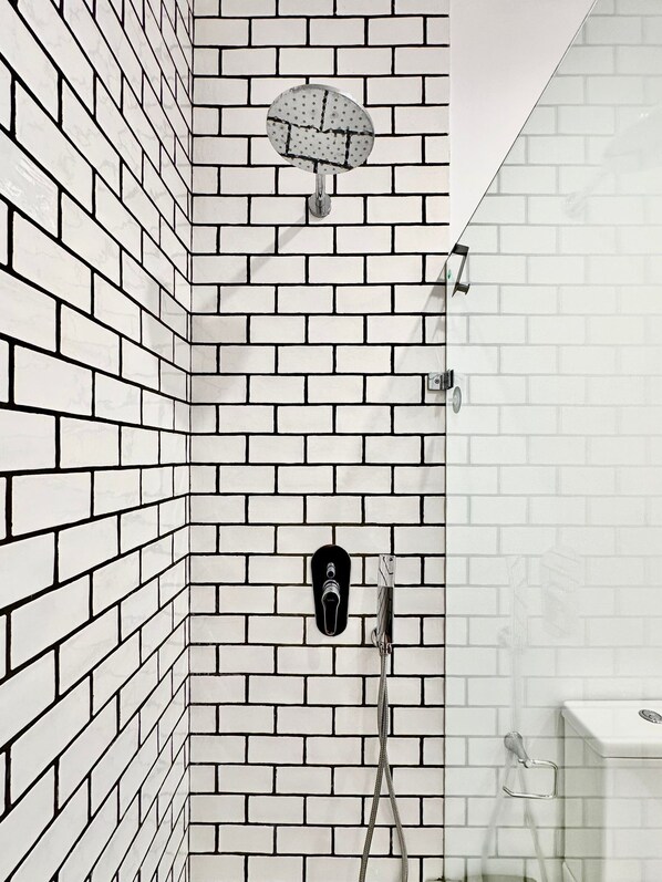 Une salle de bain avec des murs en briques blanches, une douche avec une porte en verre et des toilettes dotées d’un bidet intégré visible.