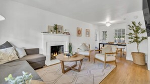 Una sala de estar con chimenea, un comedor y una cocina visibles a través de una puerta abierta.