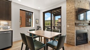 A modern kitchen with a dining area, a stone fireplace, and a large window offering a view of the outdoors. - Bf3203s2 (Silverthorne)
