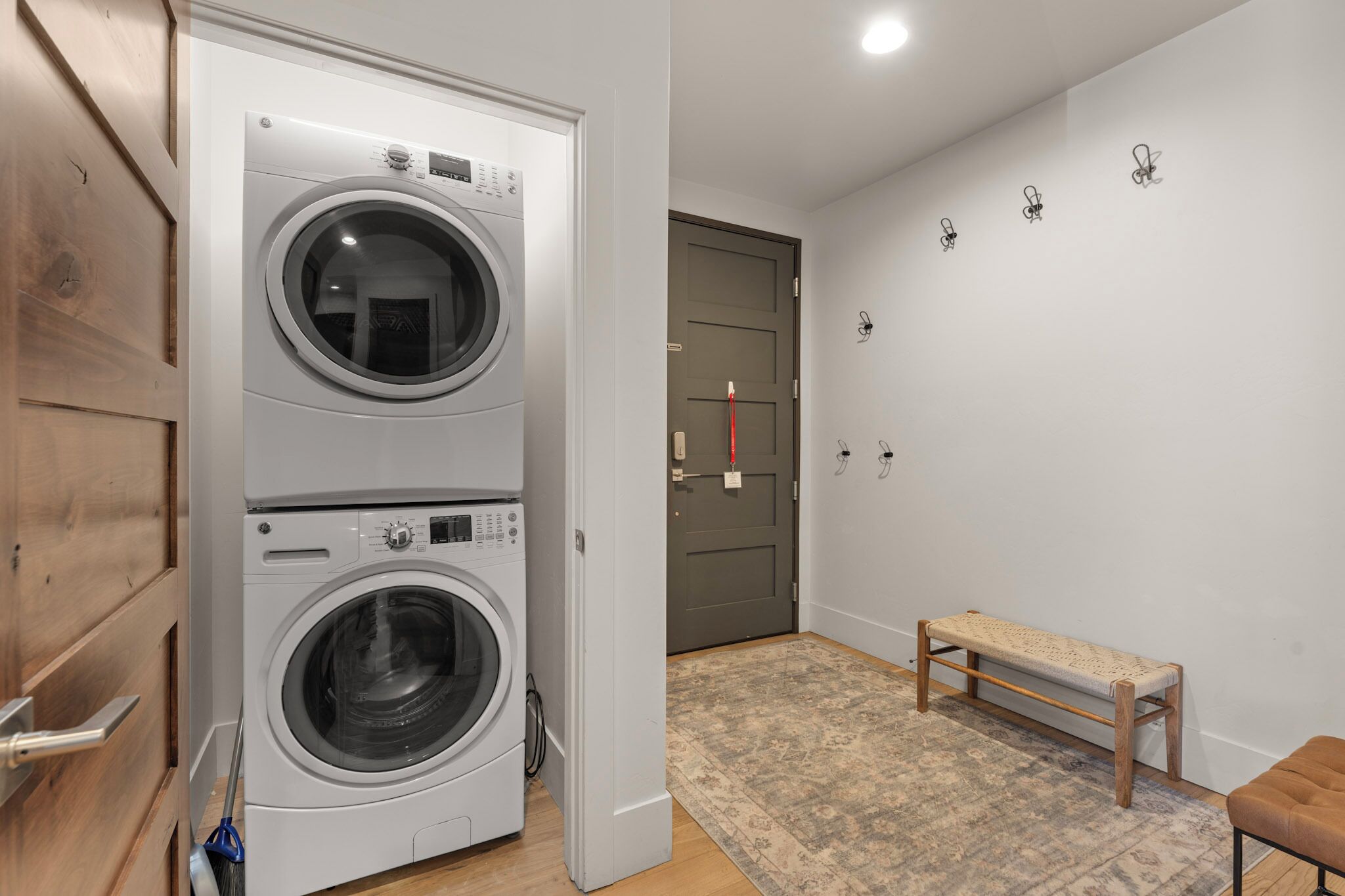 A laundry room with two stacked washing machines, a bench, and a door with a red handle.