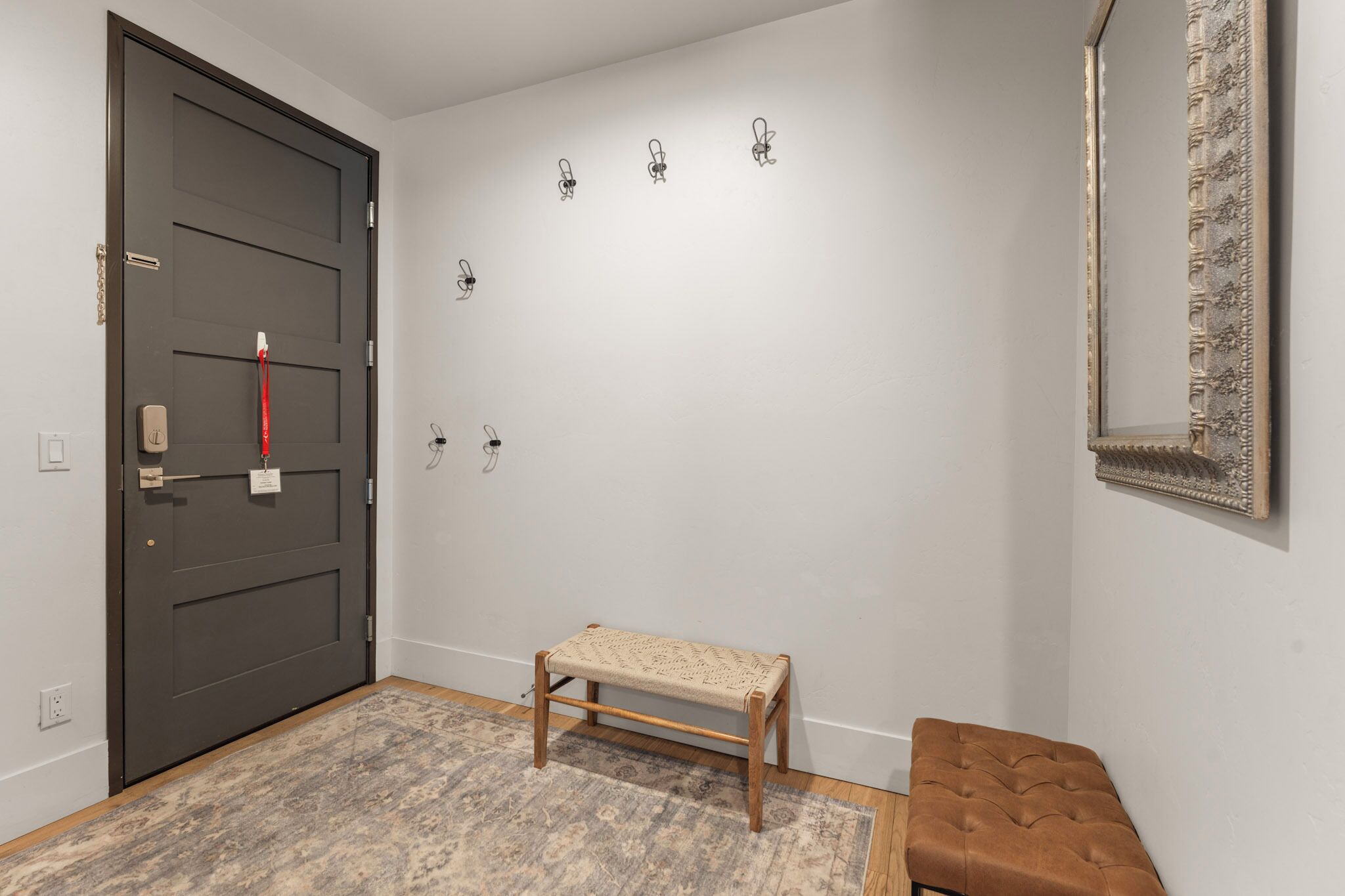 A hallway with a dark door, a bench, a patterned rug, and a wall-mounted mirror.