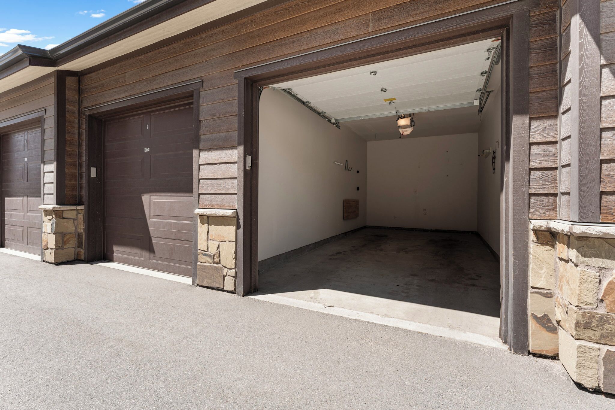 A garage with two brown doors, stone pillars, and a concrete floor.
