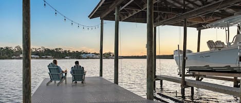 A wooden dock with two chairs and a table, overlooking a calm body of water with a boat docked nearby.