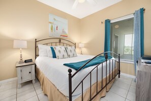 A bedroom with a bed, bedside tables, a painting, and a window with curtains.