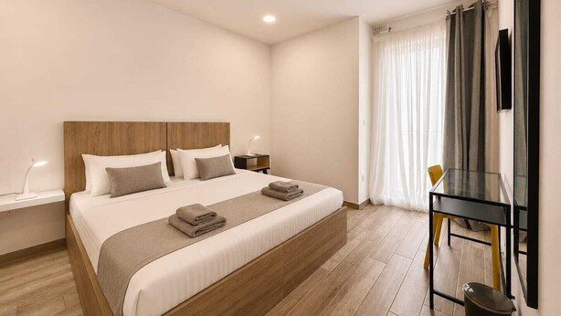 Une chambre moderne avec une tête de lit en bois, un lit avec une literie blanche, une table de chevet avec une lampe et un bureau avec une chaise.