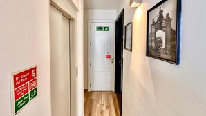 Un couloir avec un panneau indiquant la sortie de secours, un tableau encadré accroché au mur et un panneau invitant à utiliser les escaliers en cas d’incendie.