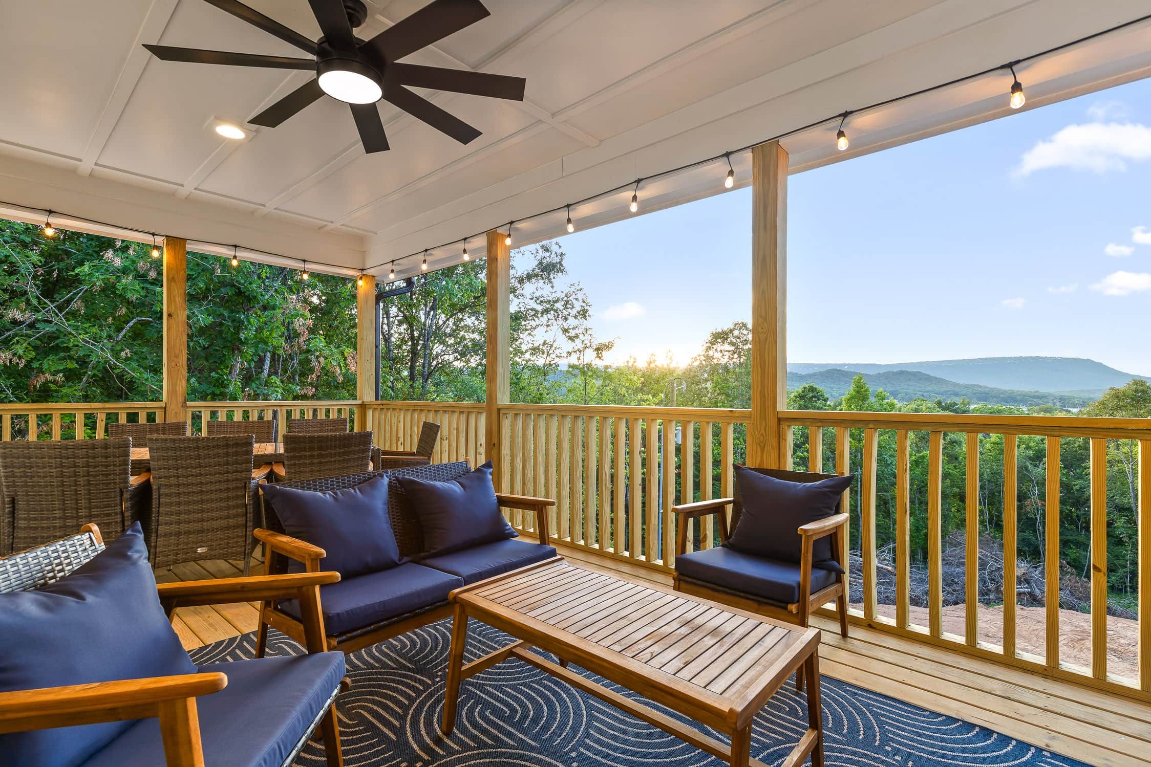 A covered outdoor seating area with a ceiling fan, string lights, and a view of the surrounding landscape.