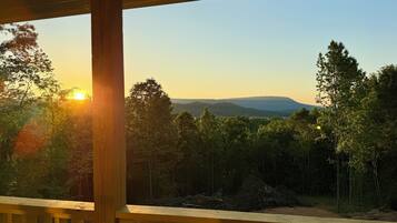 A wooden deck with a view of a forest and distant hills during sunset.