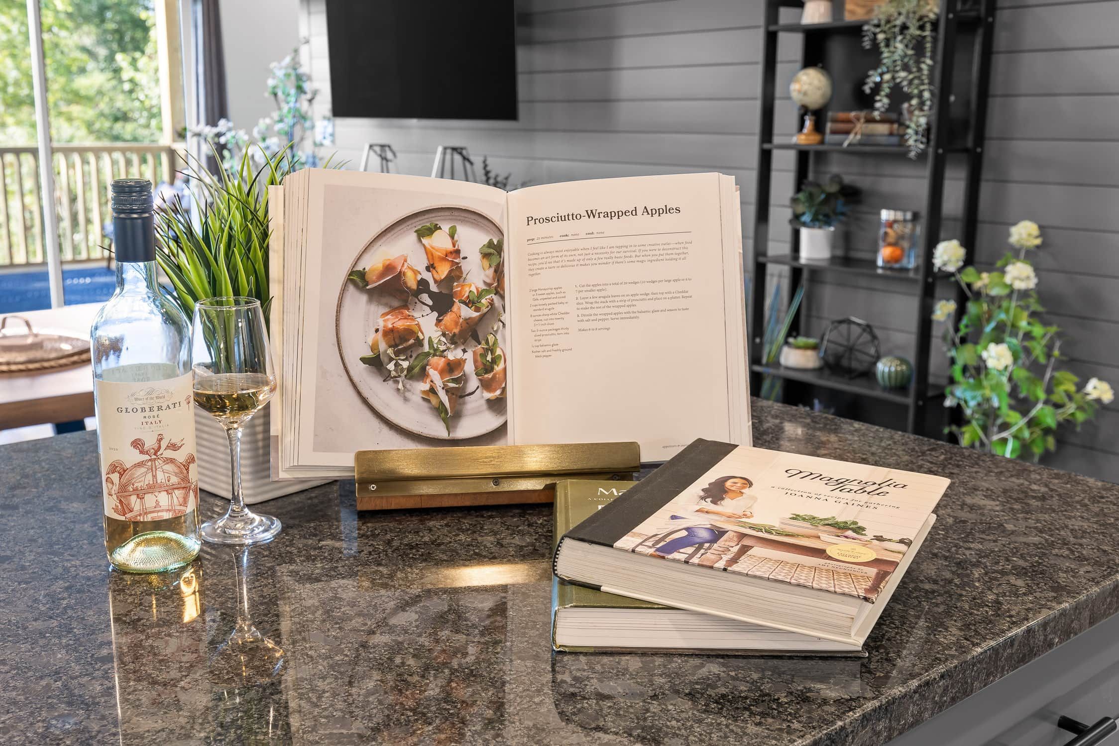 A kitchen counter with a cookbook, a wine bottle, and a glass.