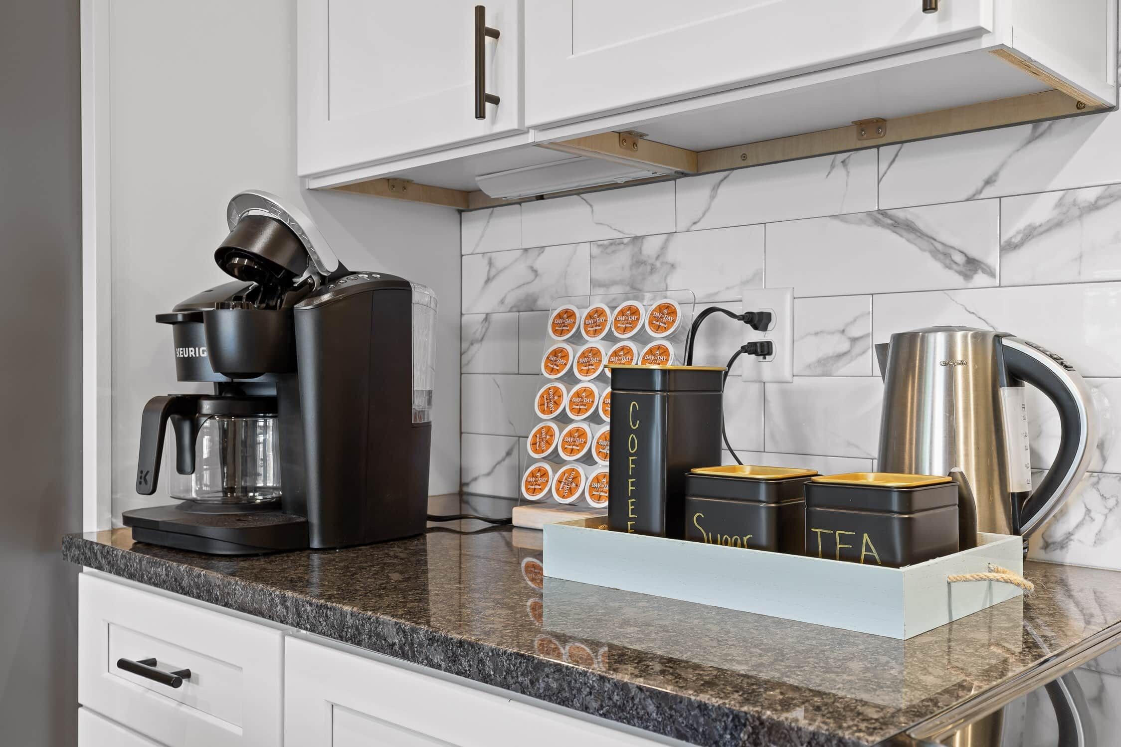 A kitchen with a coffee maker, tea containers, and a kettle on the counter.