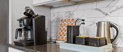 A kitchen with a coffee maker, tea containers, and a kettle on the counter.