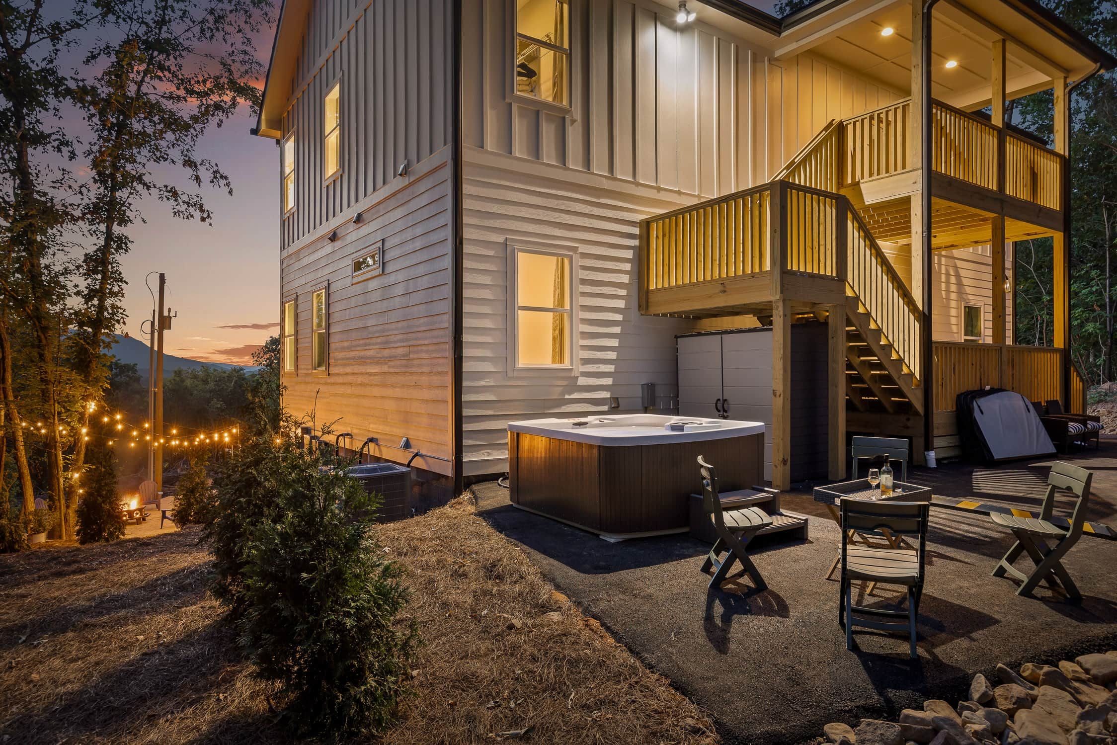 A two-story house with a hot tub, outdoor seating, and a staircase leading to a balcony.