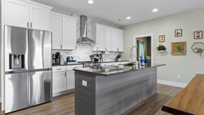 A modern kitchen with white cabinets, a stainless steel refrigerator, a large island with a sink, and a gas stove.