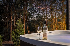 Ein Whirlpool mit Flasche und Glas auf einer Ablage, umgeben von Bäumen.