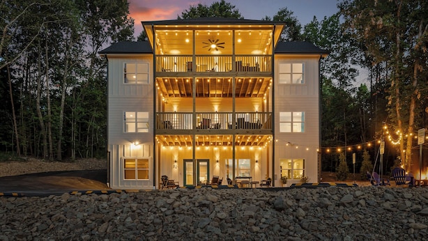 Un bâtiment à deux étages doté d’un balcon à l’étage supérieur, d’un espace extérieur couvert aménagé en coin salon et de guirlandes lumineuses.