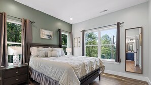 Une chambre avec un grand lit, une table de chevet, une fenêtre avec des rideaux et un miroir au mur.