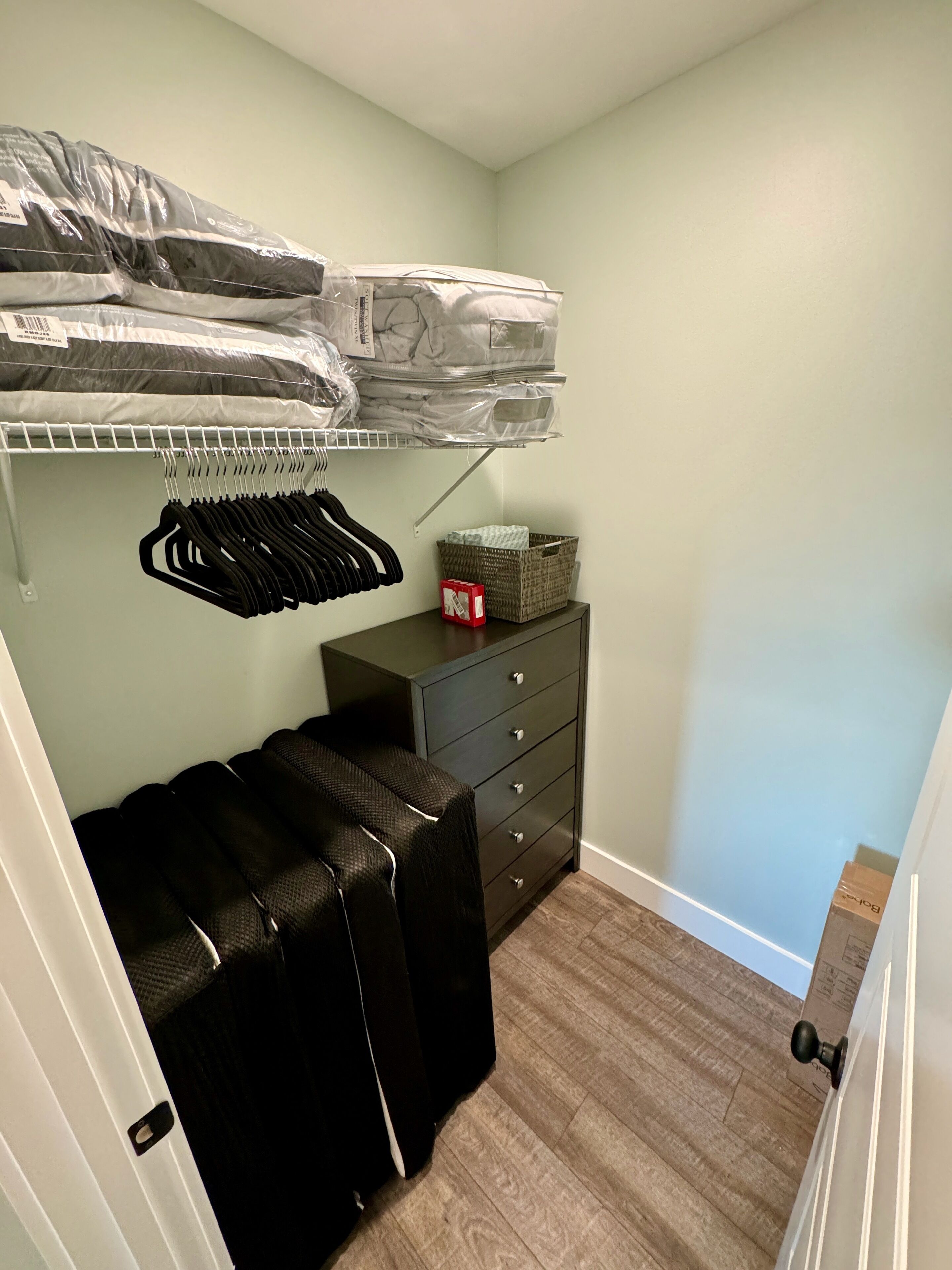 Une petite pièce avec un lit superposé, une commode et un placard où sont suspendus des vêtements.