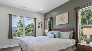 A bedroom with a large bed, a wooden headboard, a nightstand with a lamp, and a window with curtains.