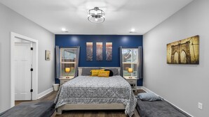Een slaapkamer met een bed, nachtkastjes, een bankje en kunstwerken aan de muur.