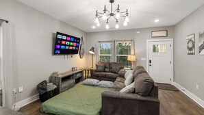 Een moderne woonkamer met een flatscreen televisie, een kroonluchter, een bank en een groene sprei op het bed.