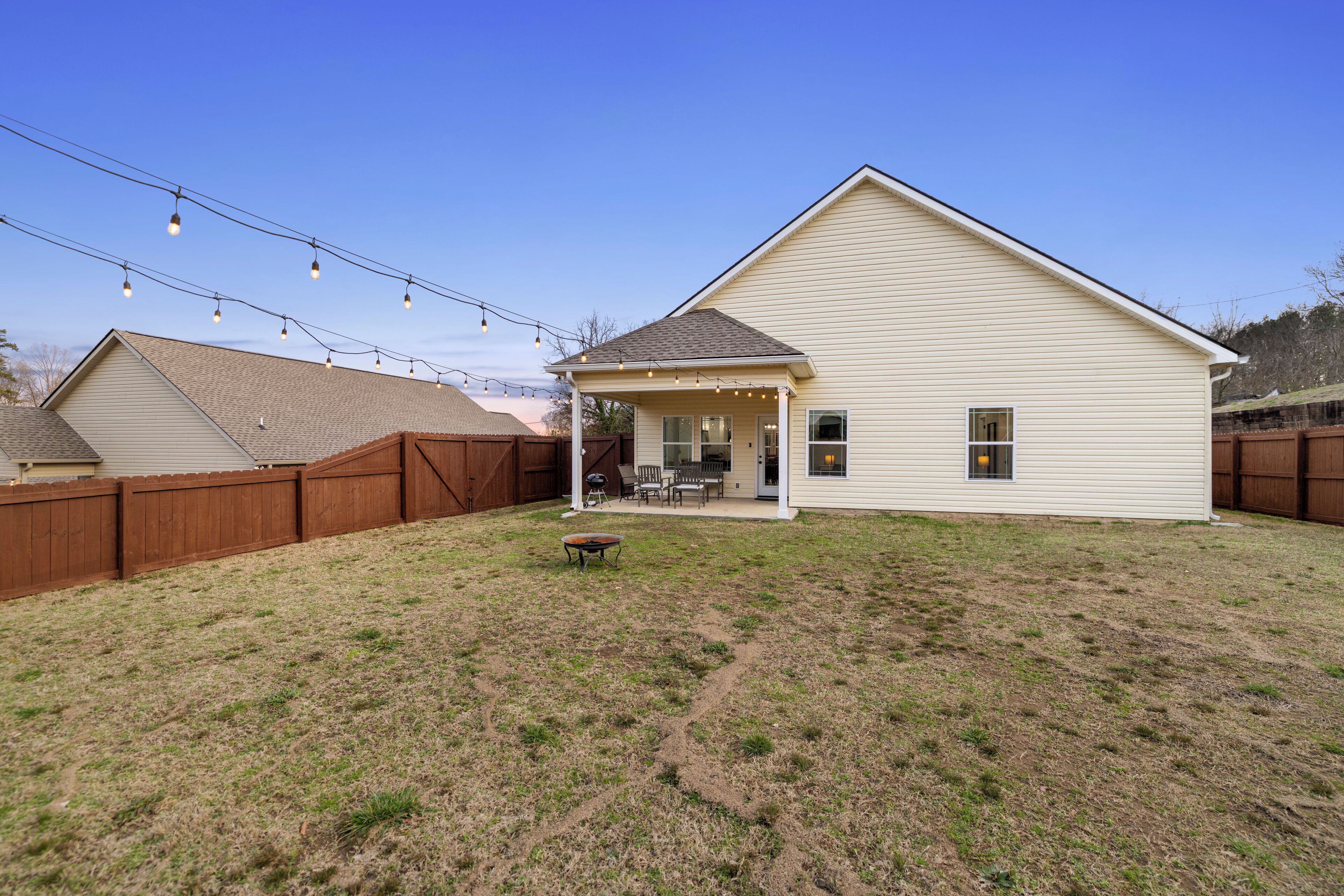 A single-story house with a covered patio area, a fenced backyard, and string lights.