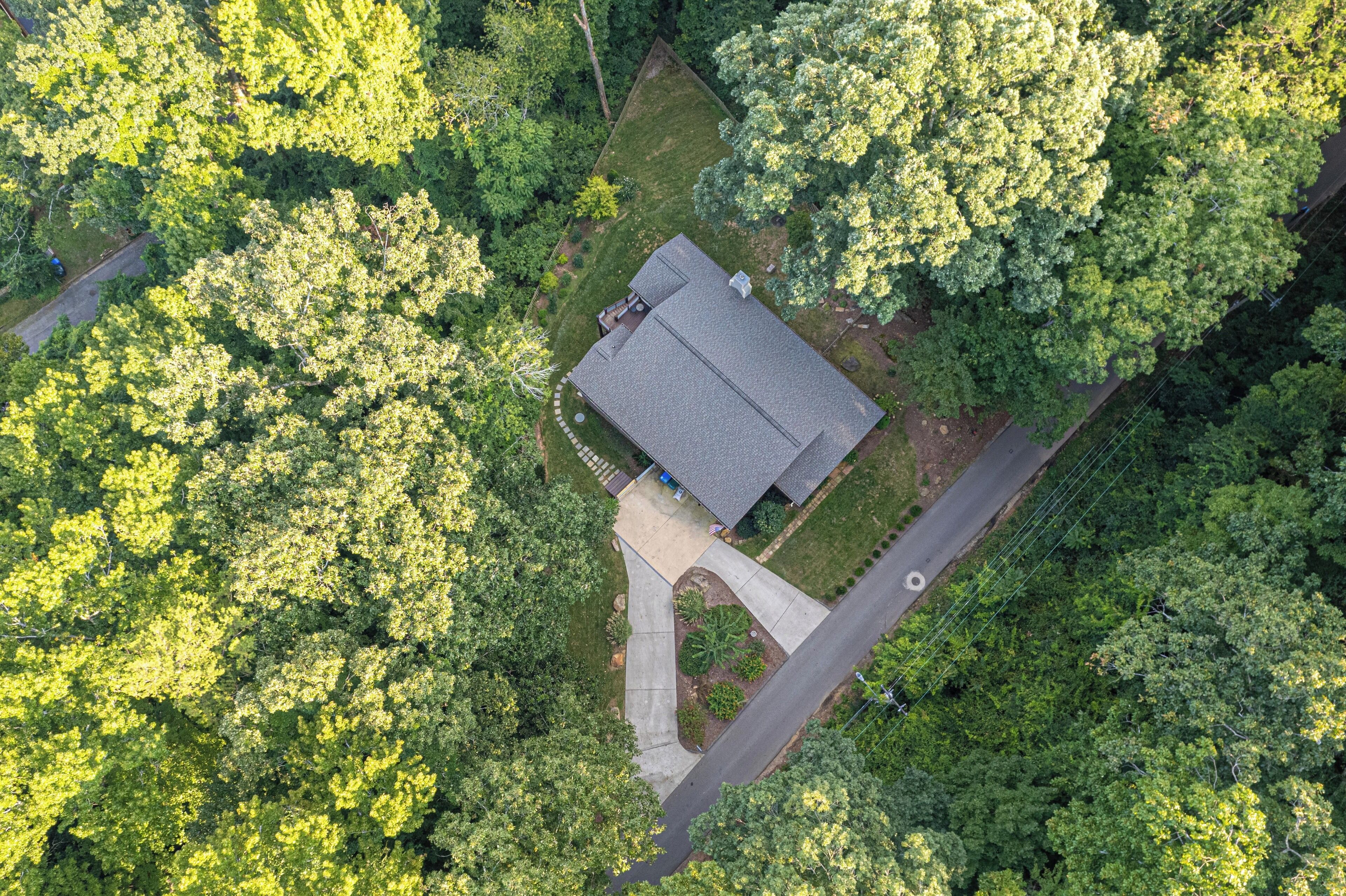 Eine Vogelperspektive zeigt ein Haus, das von dichten Bäumen umgeben ist, mit einer auffälligen Auffahrt und einem kleinen Garten.