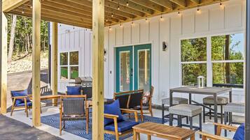 An outdoor patio with wooden furniture, a grill, and a view of the surrounding trees.