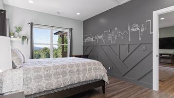 A bedroom with a bed, a cityscape wall mural, a window with curtains, and a TV in the adjacent room.
