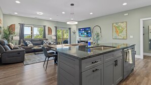 A modern kitchen with grey cabinets, a large island, and a dining area with a sofa and chairs.