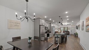 Eine moderne Küche mit Edelstahlgeräten, ein Essbereich mit einem dunklen Holztisch und einer Kronleuchter.