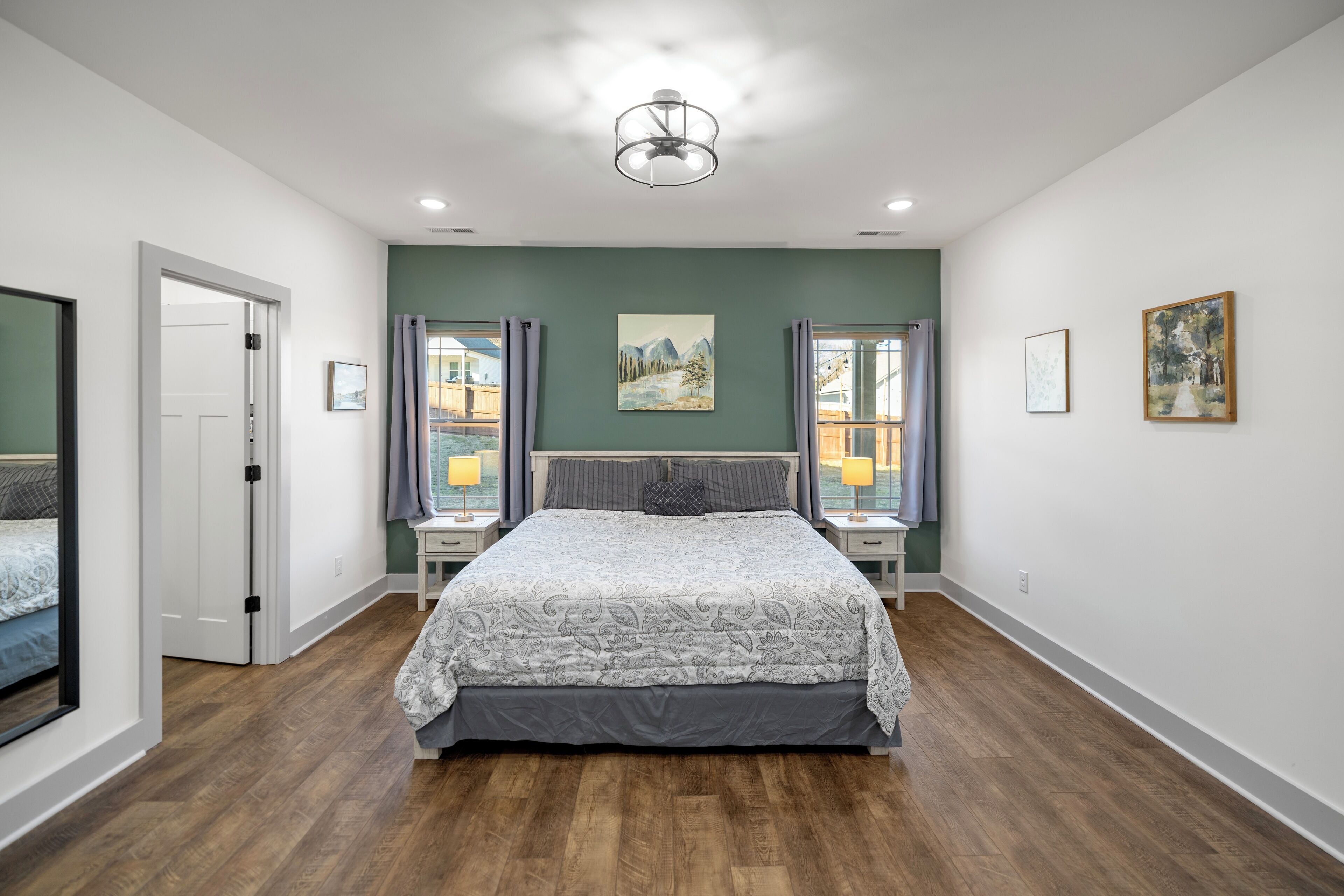 A bedroom with a large bed, two bedside tables with lamps, a ceiling light, and a painting on the wall.