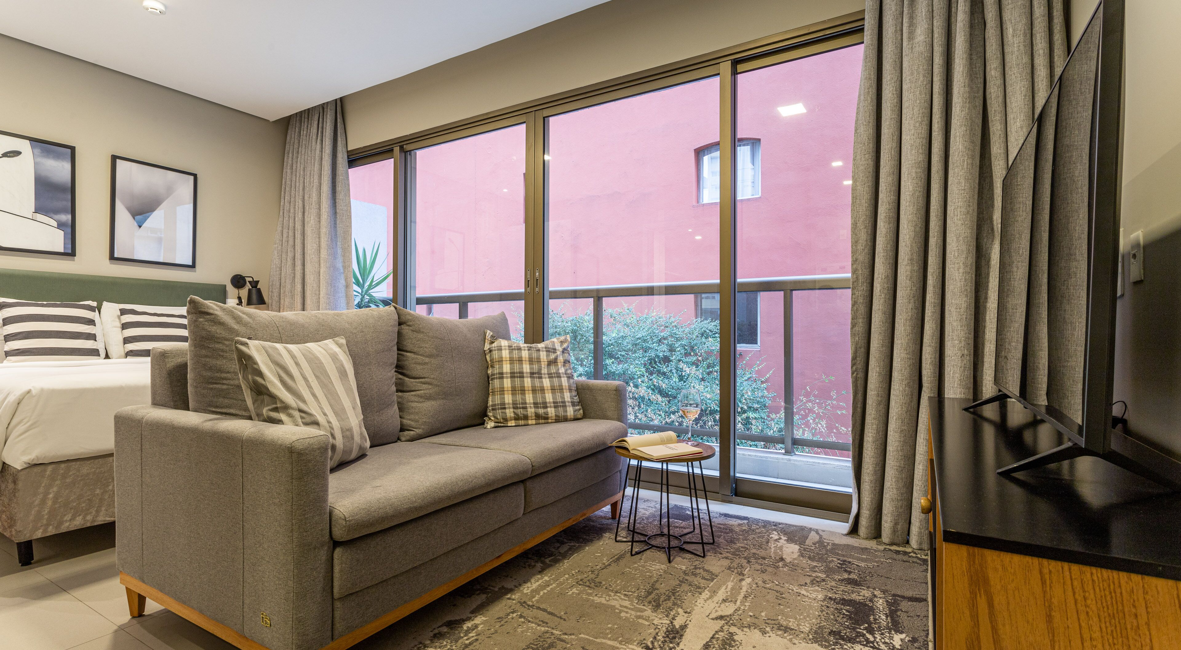 A modern hotel room with a grey sofa, a small side table, and a bed with striped pillows.