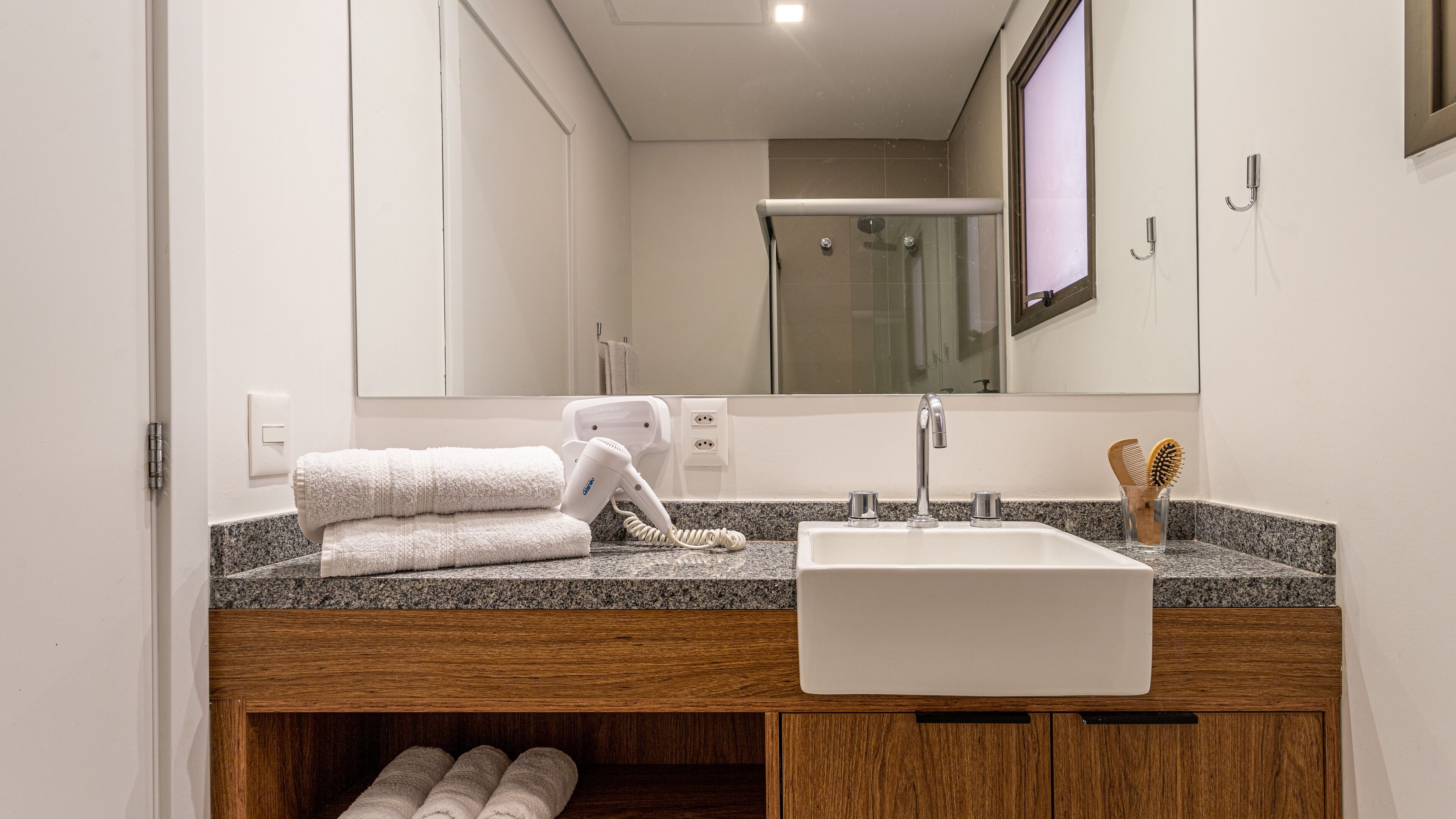 A modern bathroom with a granite countertop, a white sink, a hairdryer, and a mirror.