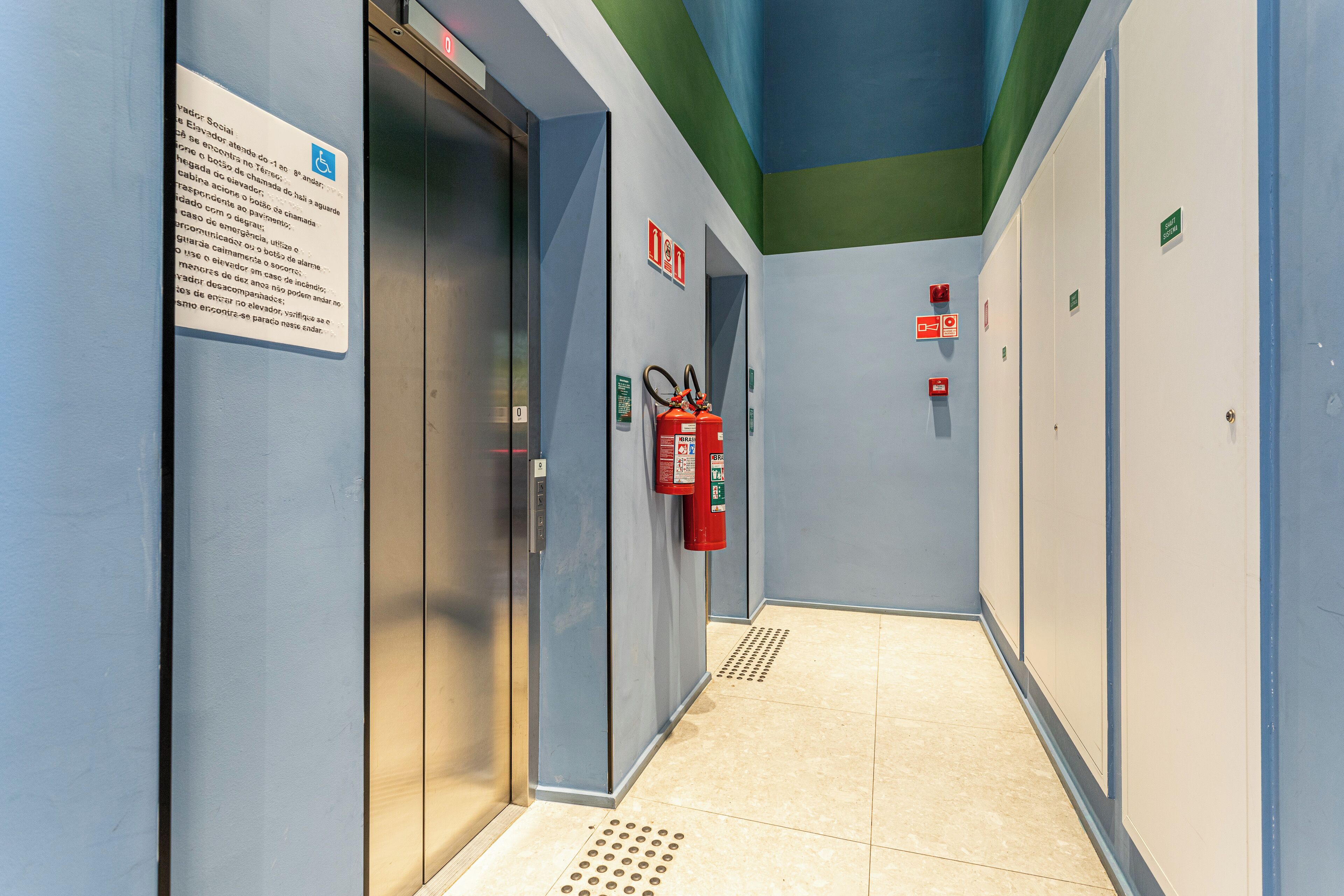 Un espace d’ascenseur équipé d’un extincteur, d’un panneau indiquant la sortie de secours et d’un panneau signalant l’accessibilité pour les personnes en fauteuil roulant.