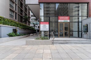 Ein modernes Gebäude mit Glastür, einer Treppe und einer angelegten Grünfläche mit Pflanzen.
