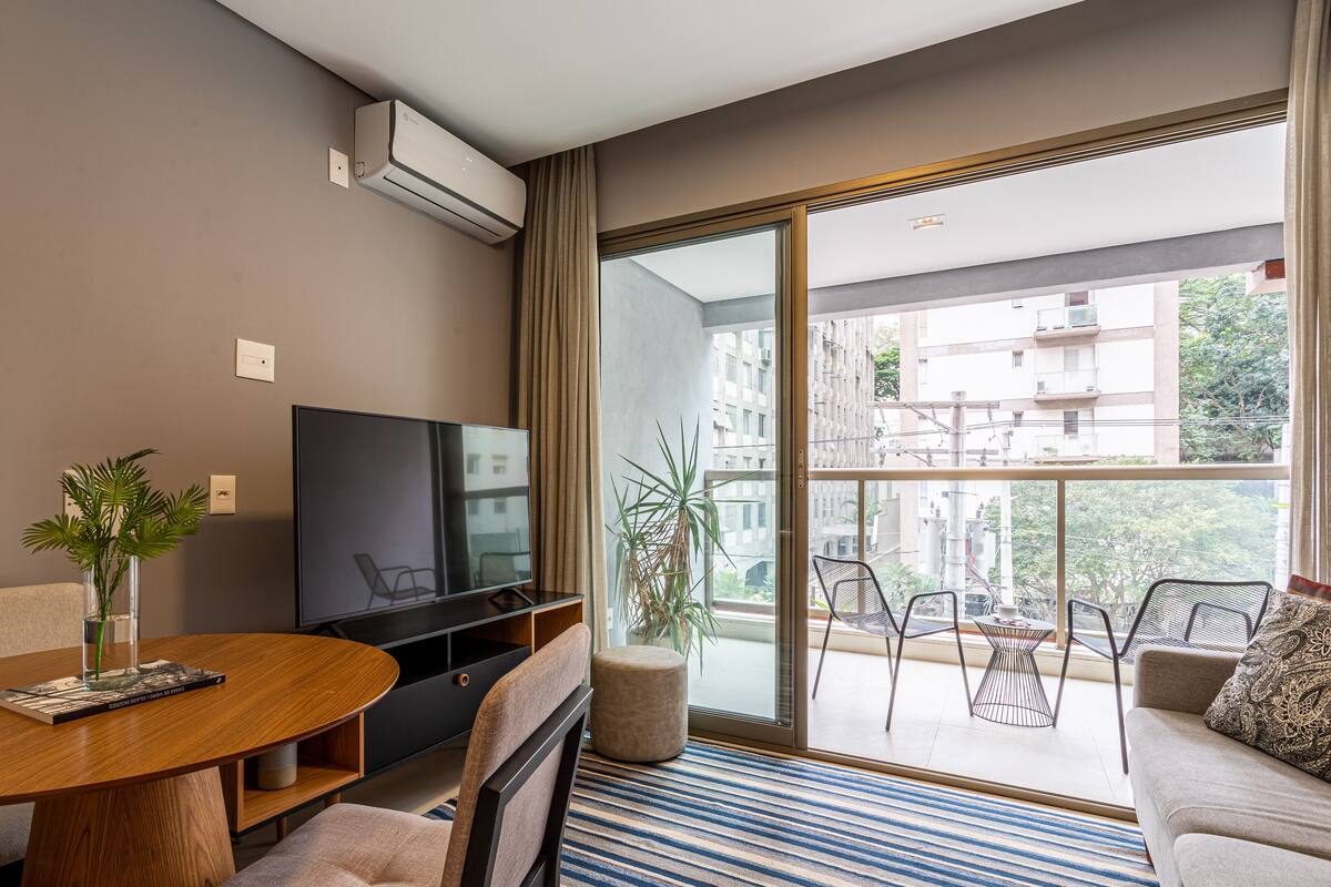 Ein modernes Wohnzimmer mit Flachbildfernseher, einem runden Holztisch, einer Couch und einem Balkon mit Sitzgelegenheit.