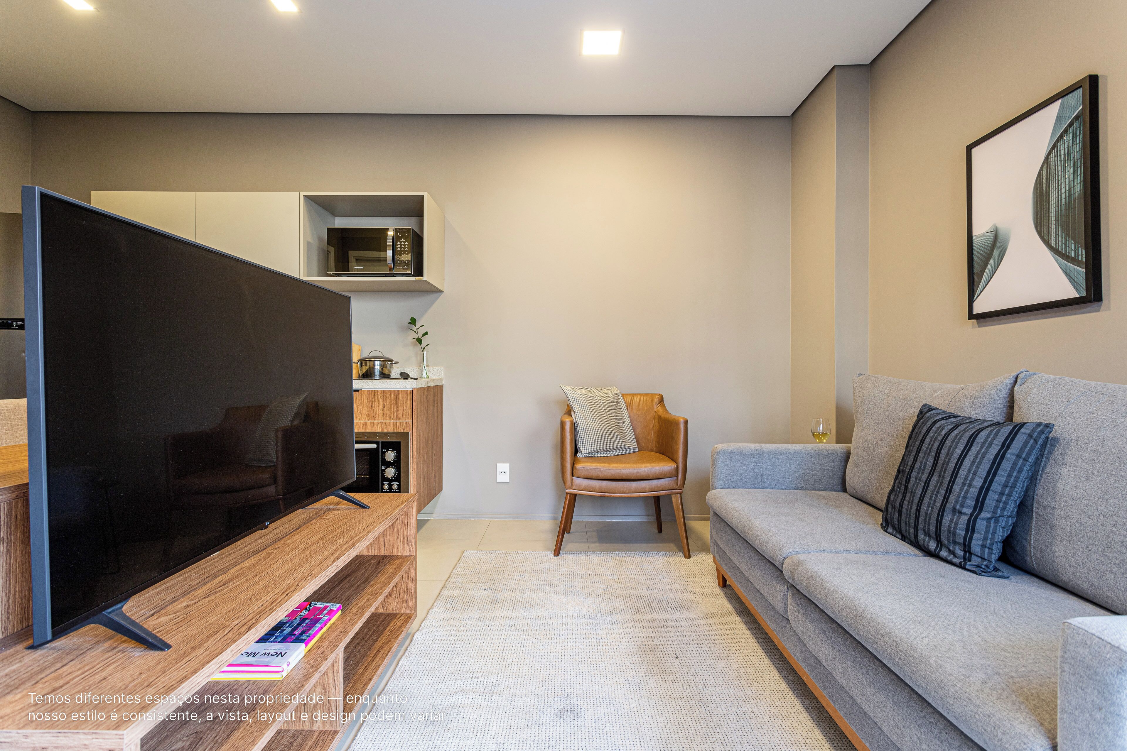 Uma sala de estar moderna com televisão de tela plana, um sofá cinza, uma mesa de centro de madeira e uma pequena mesa lateral.